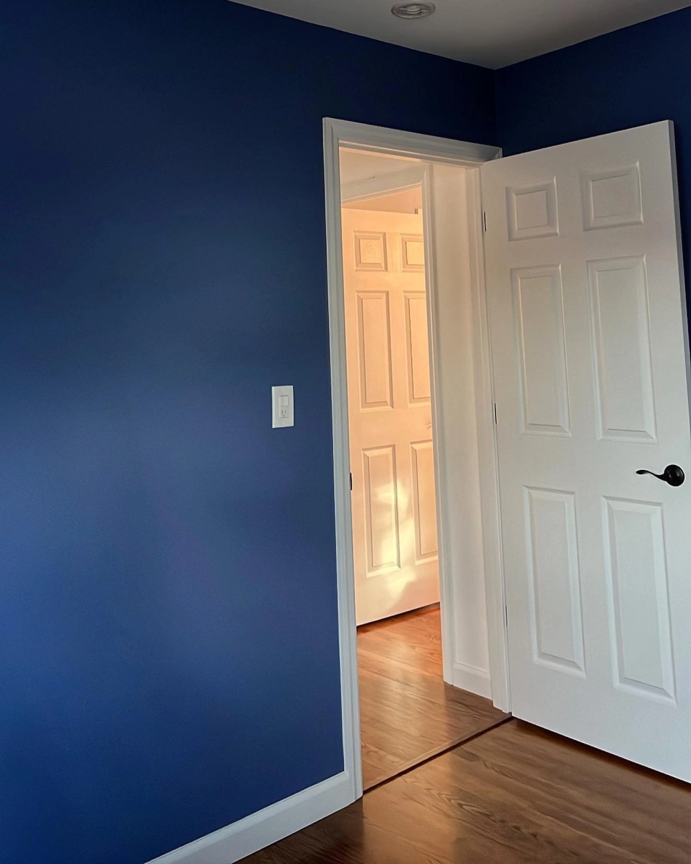 Màu sơn phòng ngủ xanh navy đậm tạo độ sâu và sự tương phản tinh tế với khung cửa màu trắng