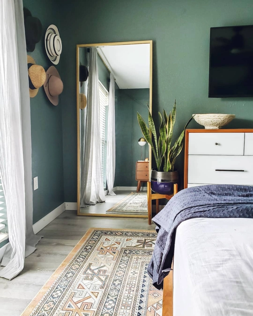 Màu sơn phòng ngủ xanh lá đậm ấn tượng kết hợp với gương đứng viền vàng và cây xanh trang trí bên cạnh tủ gỗ